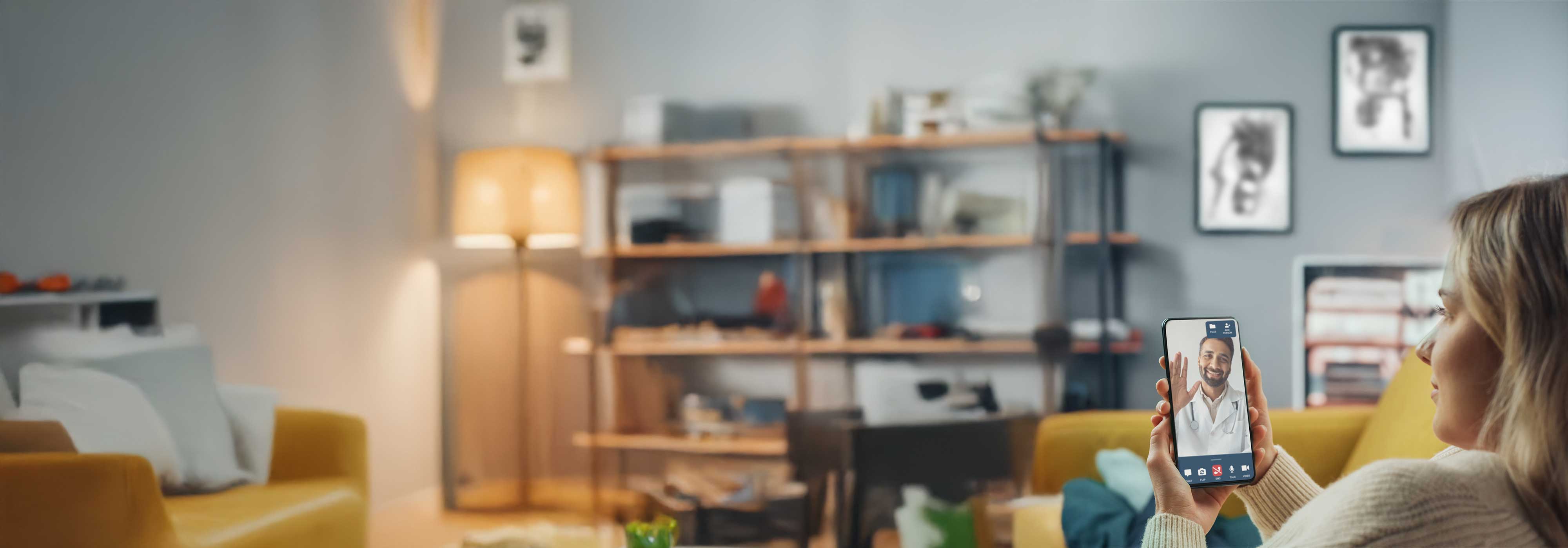 Woman sitting on yellow couch looking at phone with DialCare telemedicine visit.