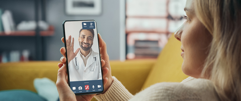 Woman sitting on yellow couch looking at phone with DialCare telemedicine visit.