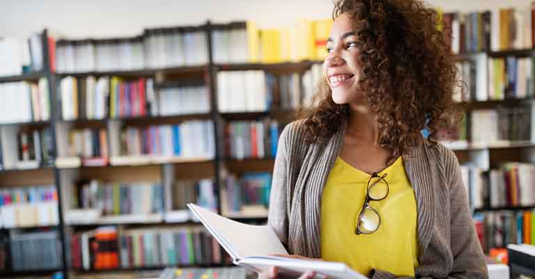 Woman with yellow shirt holding a book in a library