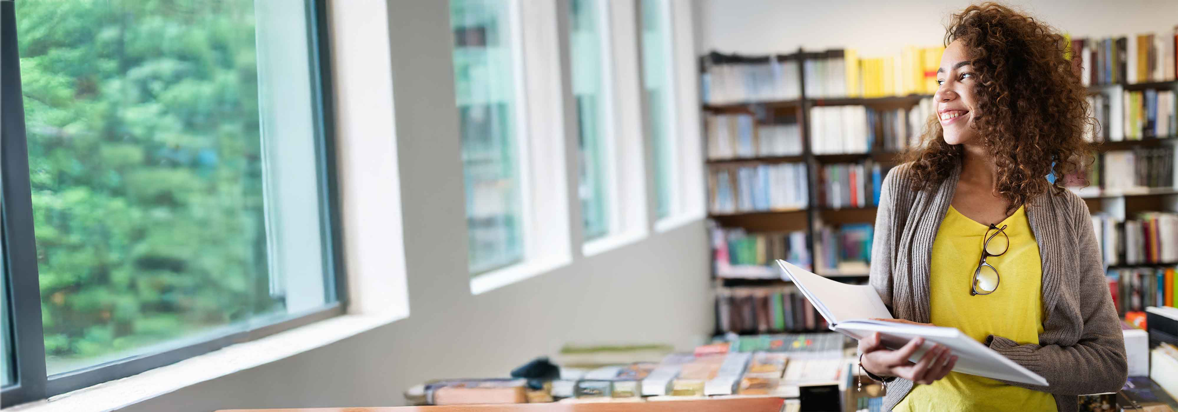 Woman with yellow shirt holding a book in a library